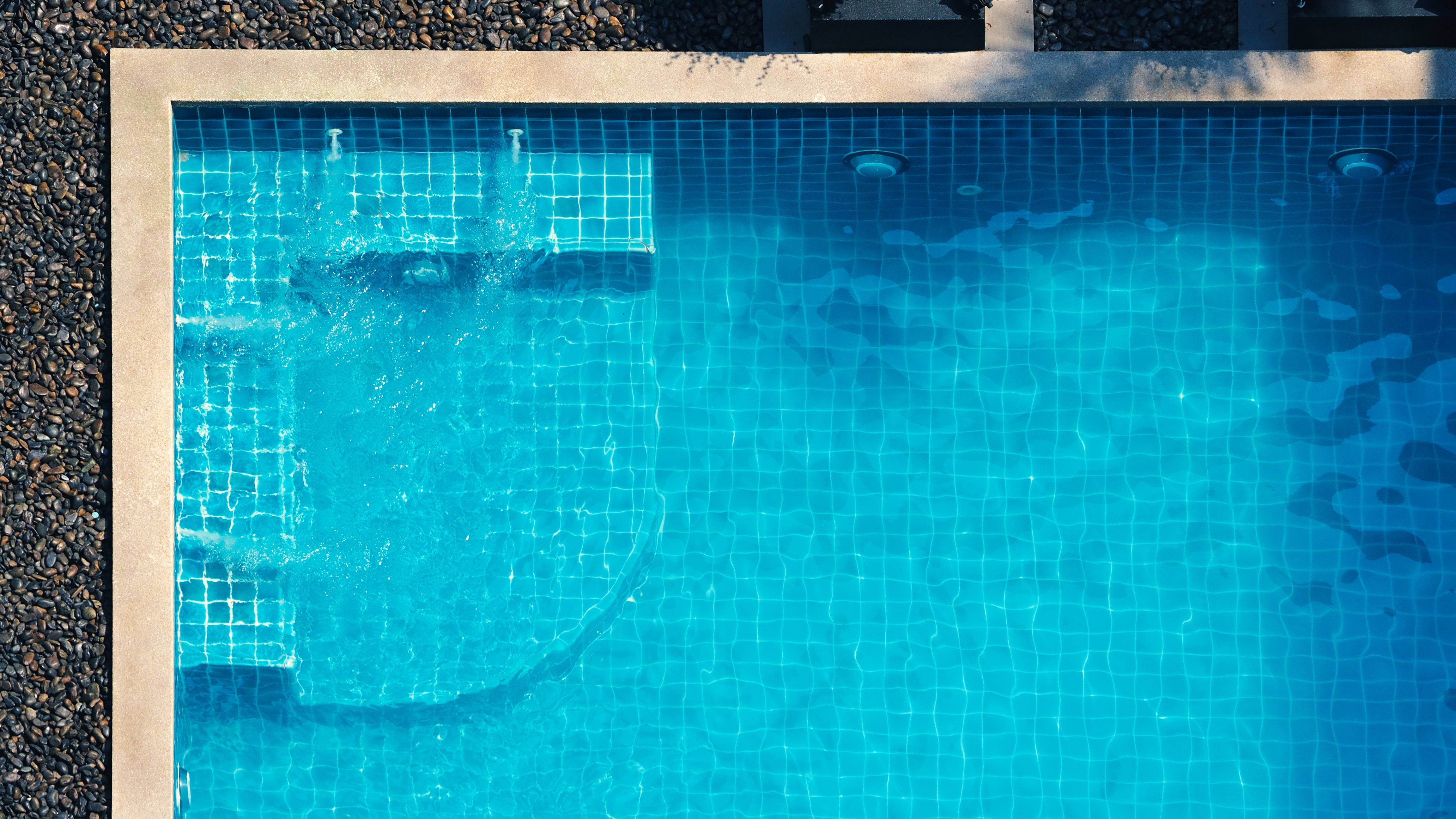 Blue mosaic glass tiles shimmering along the waterline of a modern outdoor swimming pool.