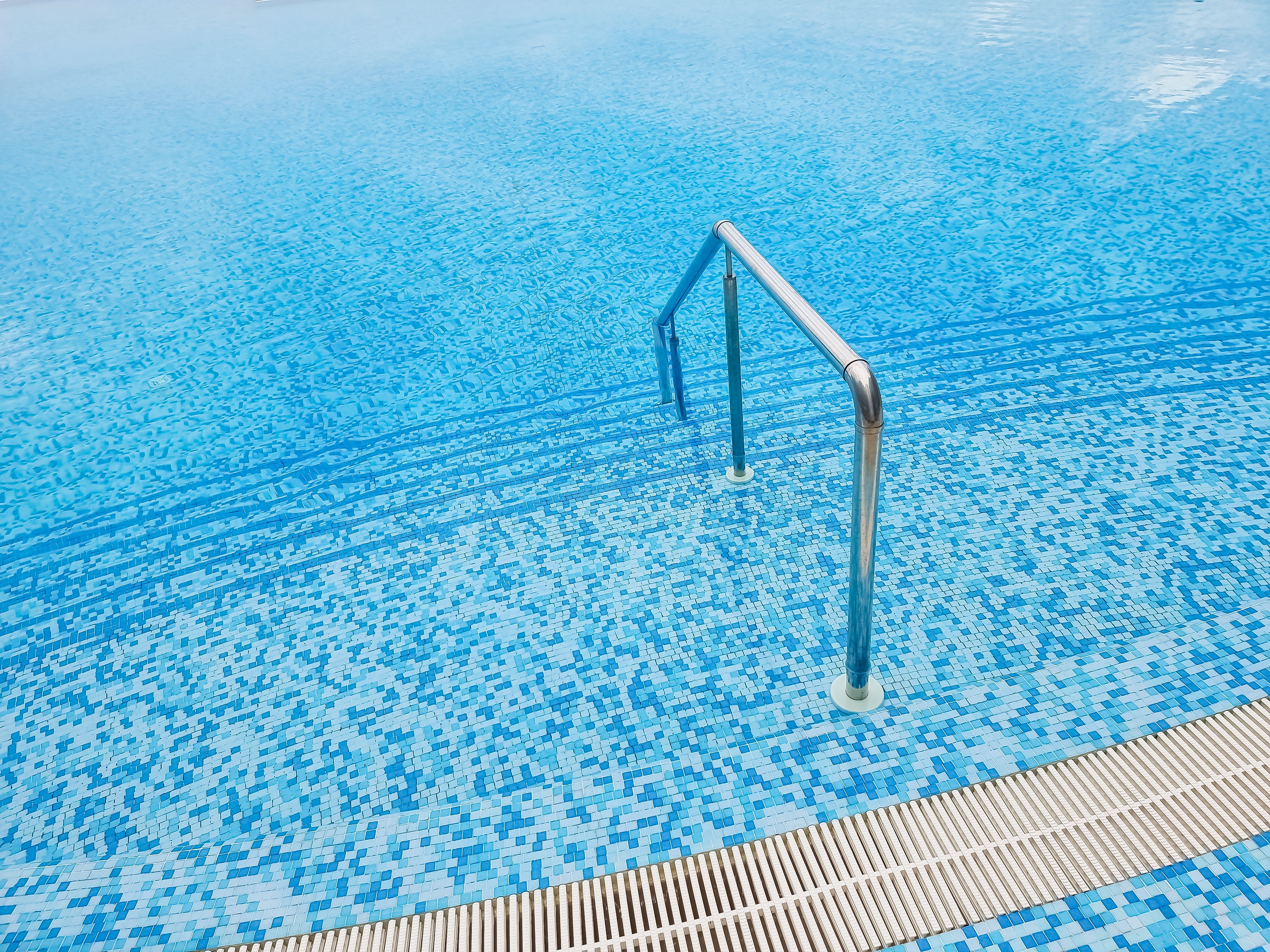 Blue pool step marker tiles highlighting steps and benches inside a clear outdoor swimming pool.