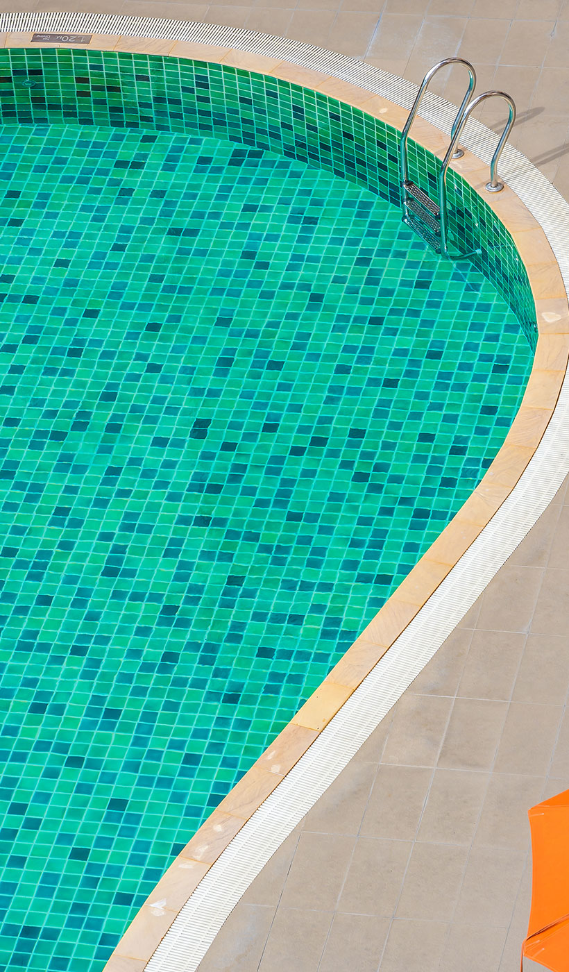 Blue glass mosaic pool tiles shimmering along the waterline of a sunlit luxury swimming pool.