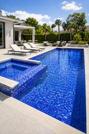 Modern backyard pool and raised spa finished in Cobalt Blue iridescent glass mosaic tile, with poolside lounge chairs.