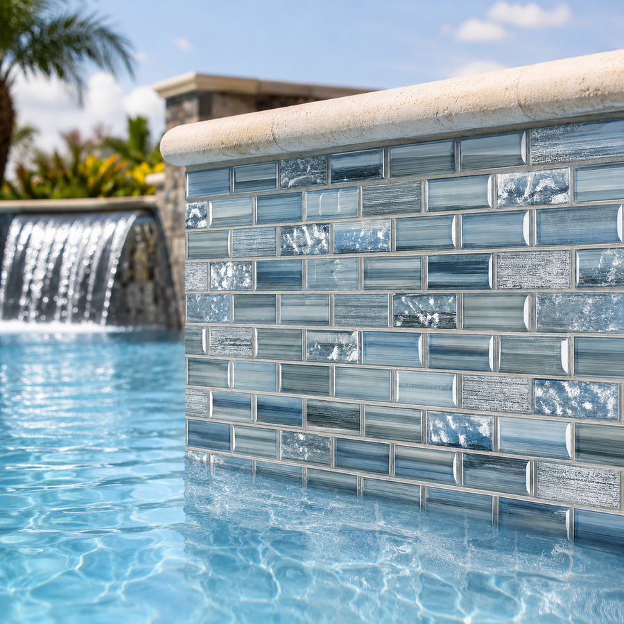 Pool with a waterfall wall clad in Linear Ocean Blend blue glass mosaic tile, framed by palms.