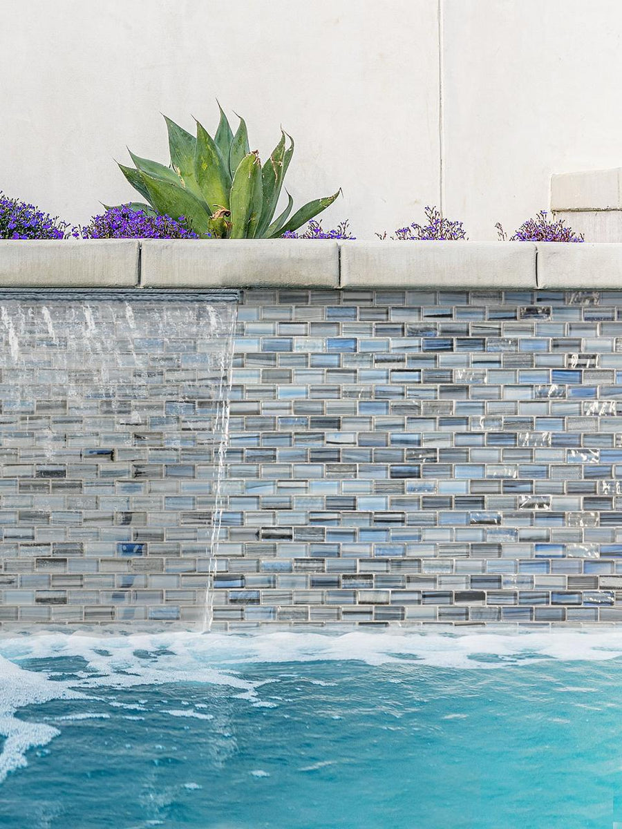 Sheer-descent waterfall over a Linear Ocean Blend blue glass mosaic wall with planters above.
