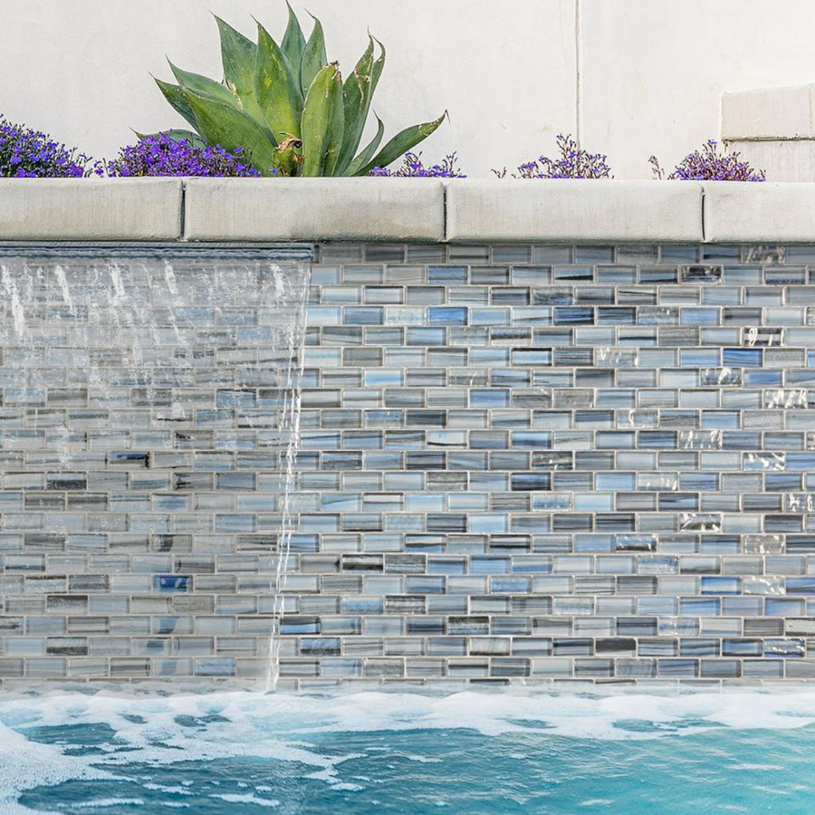 Long pool wall clad in Linear Ocean Blend blue glass mosaic tile with succulent planting above.
