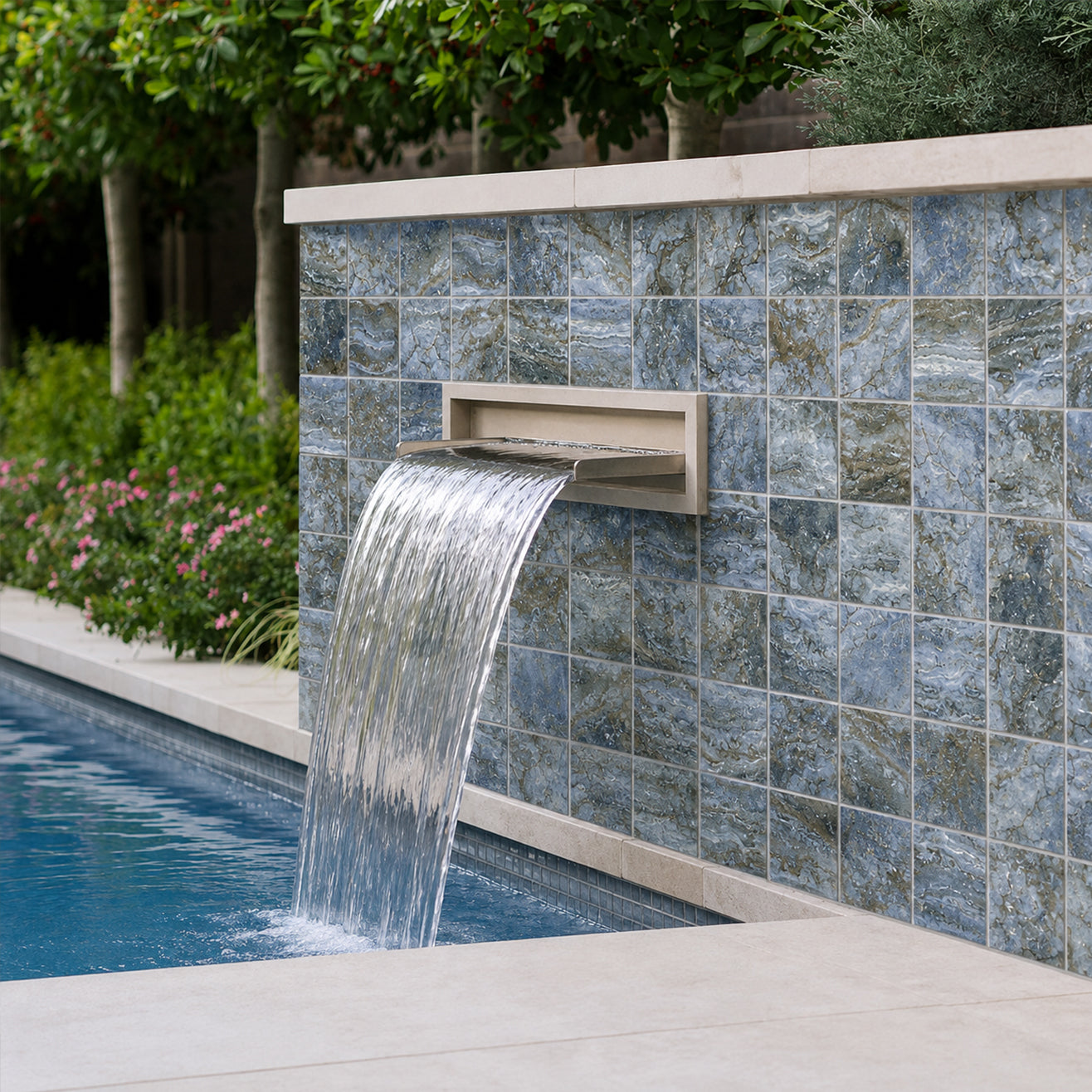 Sheer-descent water spout set into a Storm Blend blue porcelain 6x6 tiled pool wall, framed by garden planting.