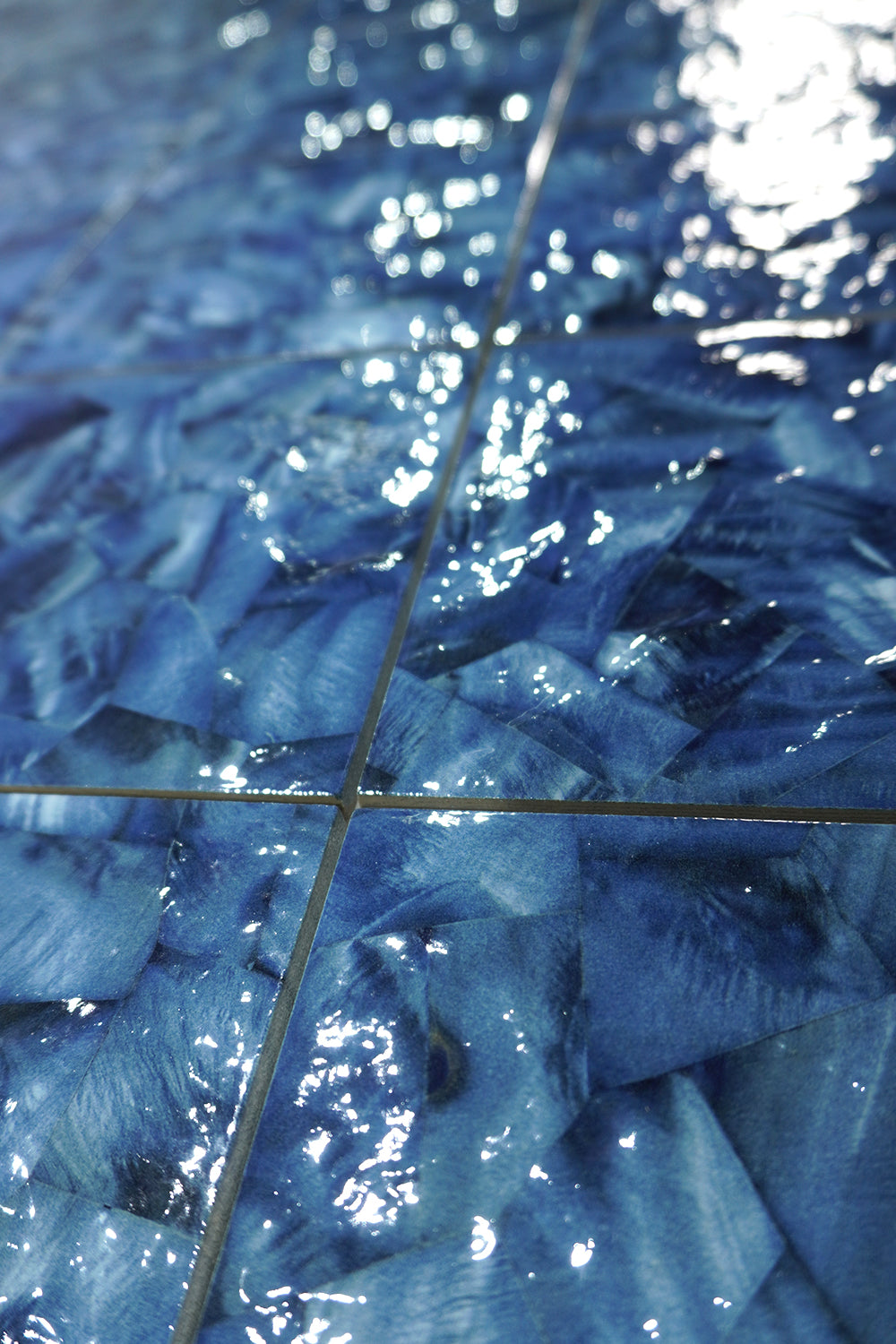 Close-up of Ocean Blue Artisan 6x6 porcelain pool tile underwater, showing brushed blue and white glaze and grout joints.