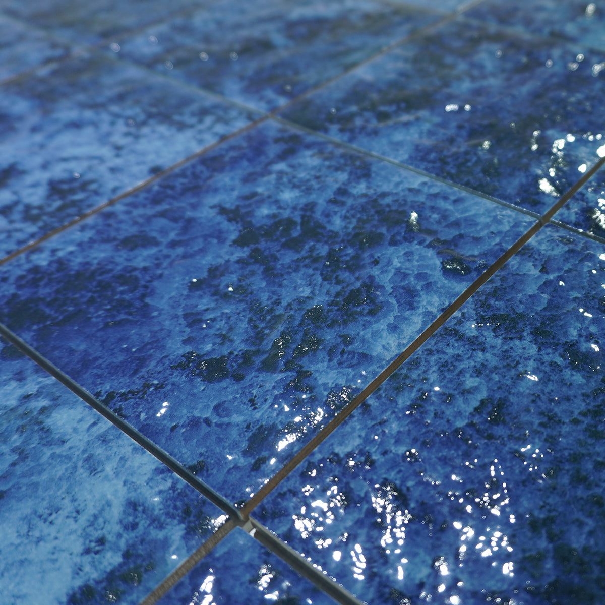 Close-up of Ocean Depth Blue 6x6 porcelain pool tile showing mottled indigo and white glaze and grout joints.