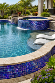 Round raised spa with curved spillway steps clad in Sapphire Indigo iridescent glass mosaic tile among tropical planting.
