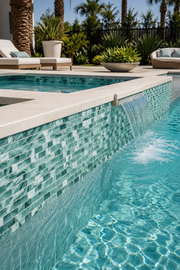 Pool with a spillway wall clad in Seafoam Green Swirl recycled glass mosaic tile beside poolside seating.