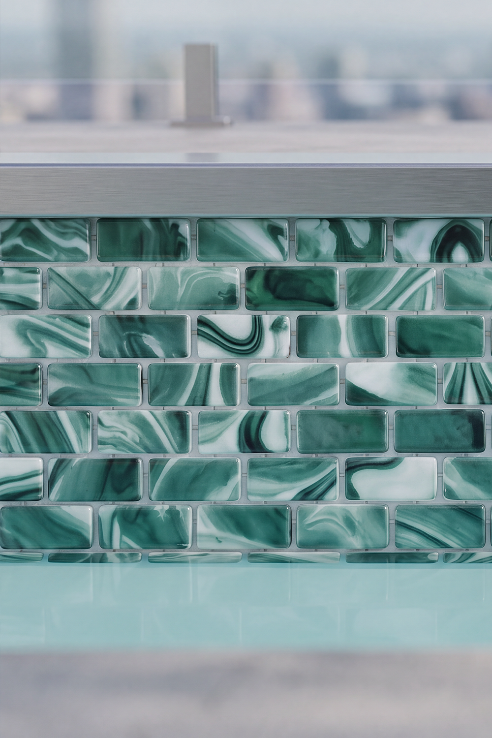 Waterline band of Seafoam Green Swirl recycled glass mosaic tile at a pool edge with a blurred city view.